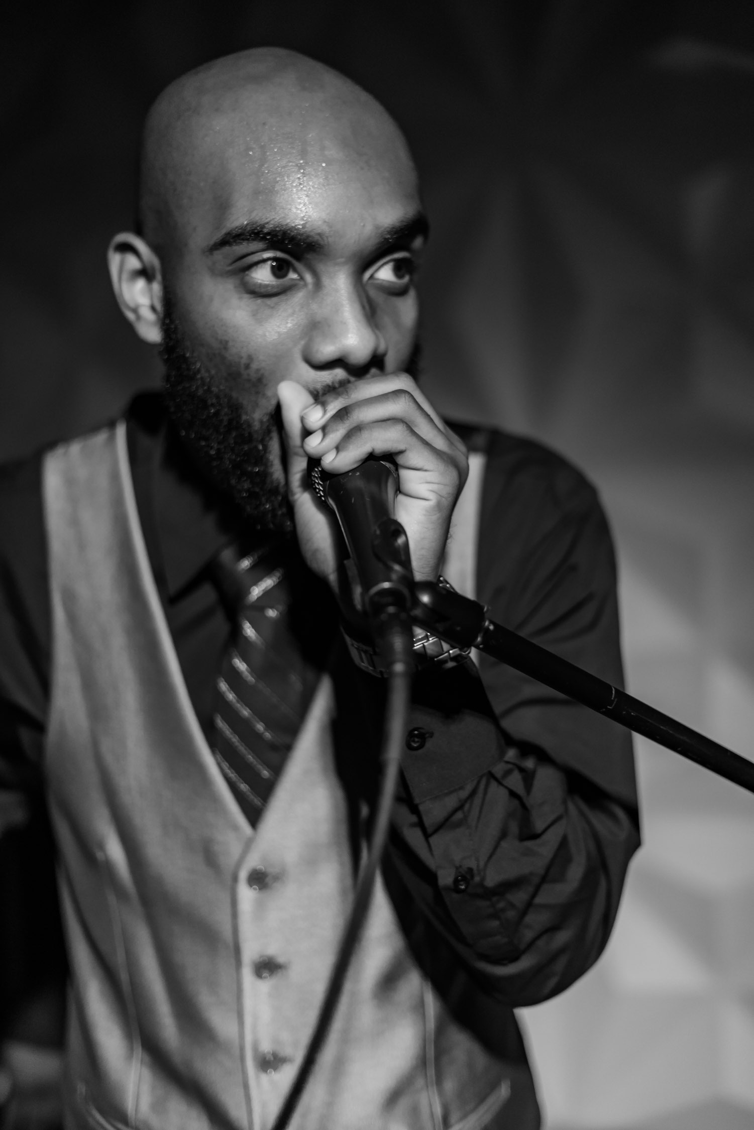 Black-and-white photograph of Radio Jamez hosting with a microphone, wearing a vest and tie